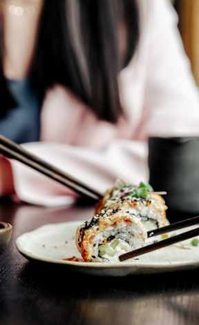 A woman is eating sushi with chopsticks.