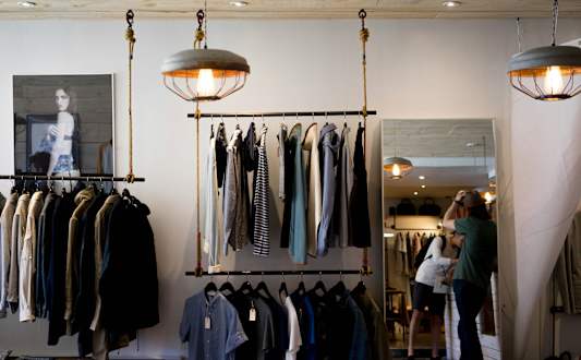 A woman is shopping in a clothing store with a variety of shirts hanging on the racks.