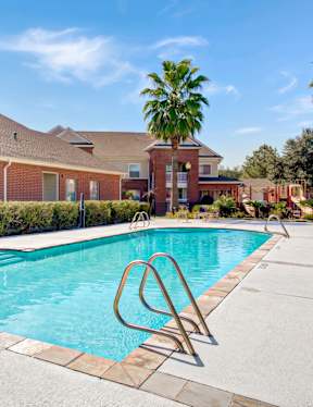 A swimming pool in front of a brick building with palm trees in the background.