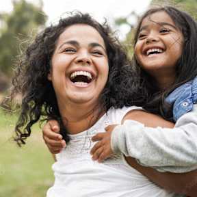 A woman and a young girl are laughing together in a park.