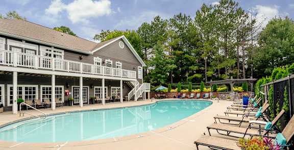 A pool area with a building and lounge chairs.
