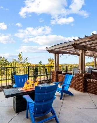 a patio with a fireplace surrounded by four chairs next to a pergola with grills.  at Vue at Westchester Commons, Midlothian, 23113