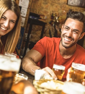 Friends at Bar Laughing and Smiling with Beers on Table 