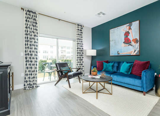A living room with a blue couch, a wooden chair, a coffee table, and a painting on the wall.