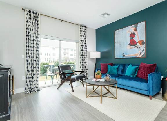 A living room with a blue couch, a wooden chair, a coffee table, and a painting on the wall.