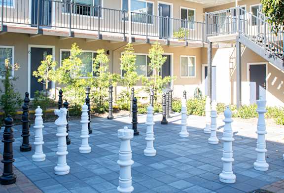 A chess set is set up on a brick patio in front of apartment buildings.