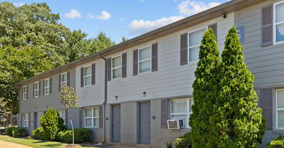 A grey apartment building with a tree in front.
