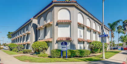 A street view of a building with a blue sign in front.