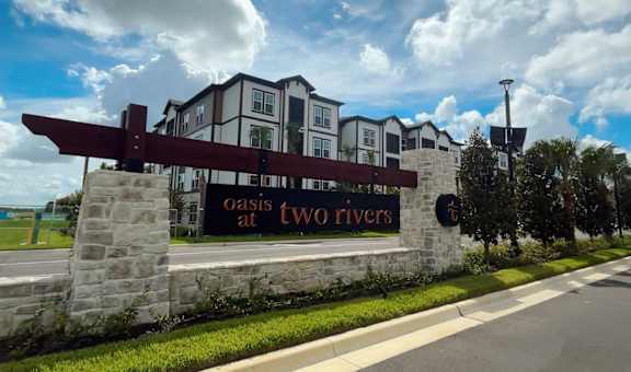 A sign for Oasis at Two Rivers is displayed in front of a building.