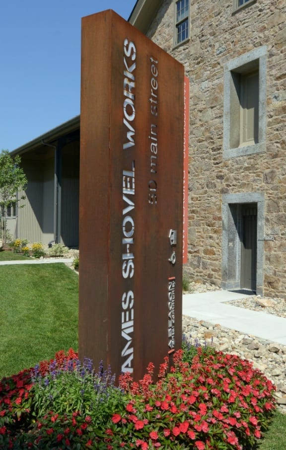 a wooden sign in front of a stone building at Ames Shovel Works Apartments in North Easton, Massachusetts 02356