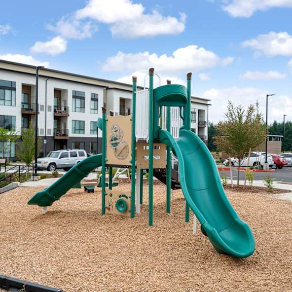 A playground with a green slide in front of a building.