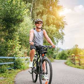 A man is riding a bicycle on a paved path in a wooded area.