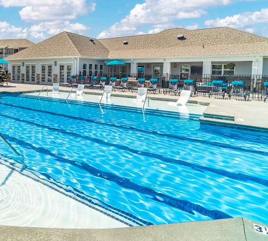 A large outdoor swimming pool with a blue tinted water and a white fence around it.