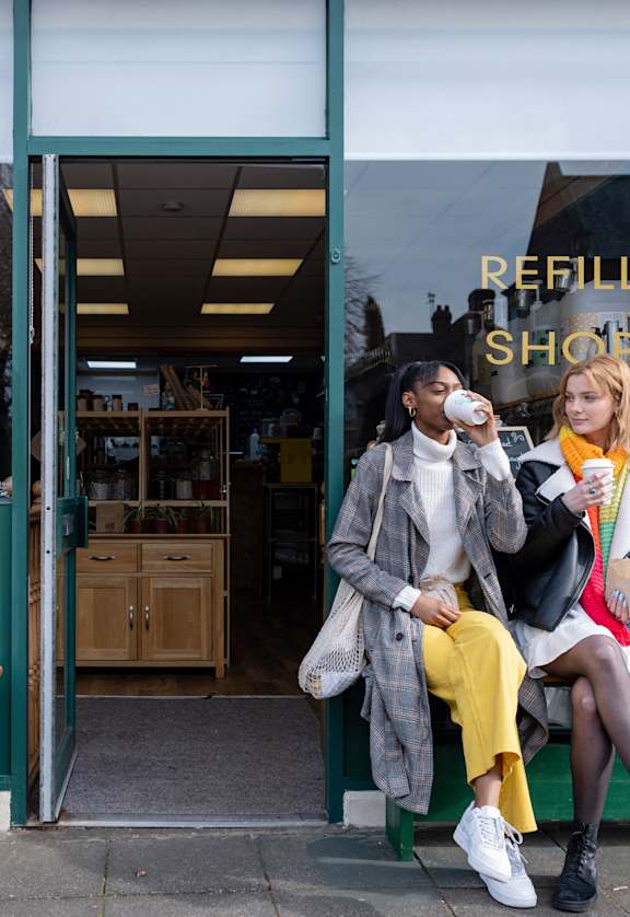 two women sitting on a bench in front of a store