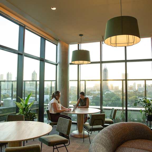 Two people sitting at a table in a room with large windows. at Scout Living, powered by Placemakr Apartments, Atlanta, GA, 30308