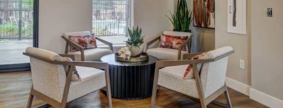 Westlake Greens' clubhouse has four modern armchairs with patterned cushions, a round black coffee table, a potted plant, and artwork.