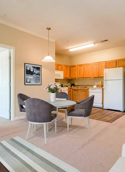 A living room with a grey sofa, a grey armchair, a coffee table, a television, and a kitchen in the background.