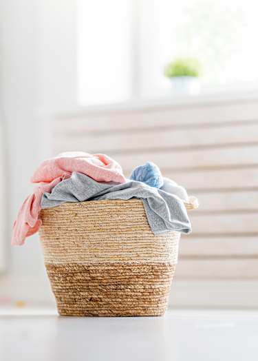 A basket with clothes is in front of a washing machine.