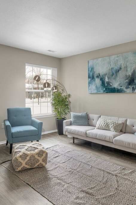 A living room with a blue chair, a white couch, and a large painting on the wall.