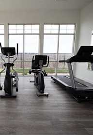 A row of treadmills and exercise bikes are lined up in a brightly lit room.