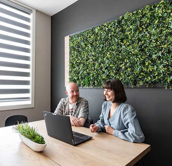Two people sitting at a table with a laptop and a plant on the table.