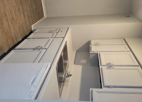 A kitchen with white cabinets and a white wall.