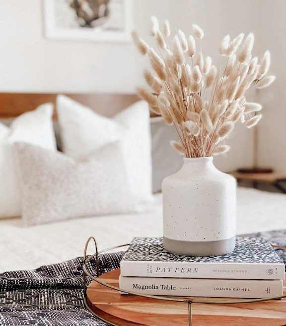 A white vase with dried flowers sits on a wooden tray with a book titled "Pattern" by Magdalena Cielecka.