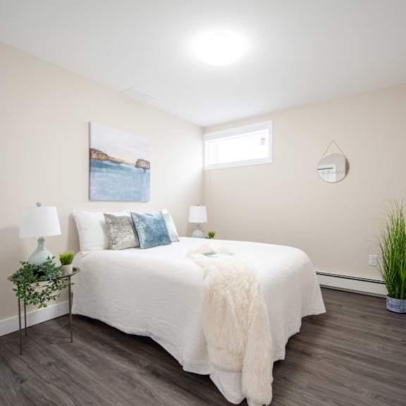 A bedroom with a large bed, a painting on the wall, and a wooden floor.