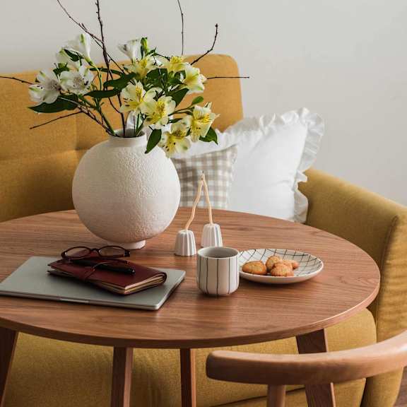 A circular brown dining table with a vase of flowers and a laptop