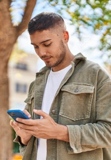 a young man texting on his cell phone in a park at The Heritage at Arlington Apartment Homes, Greenville, NC 27834