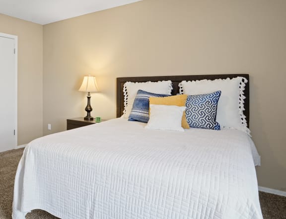 white bed with orange and blue pillows and fan above bed