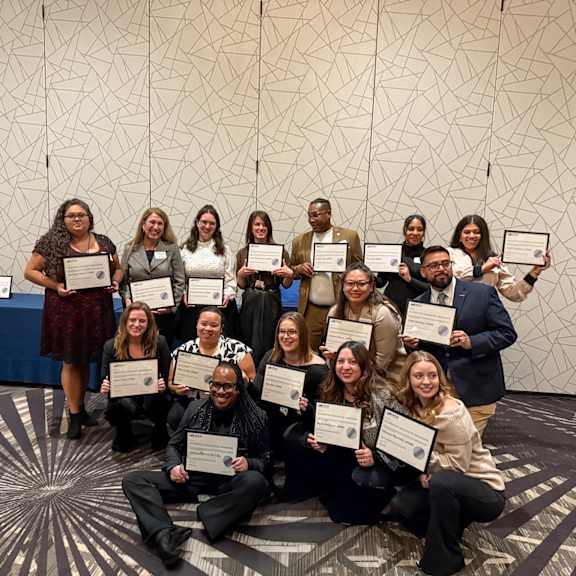 A group of people holding certificates in front of a patterned wall. at Lakes Edge Apartments, North Carolina