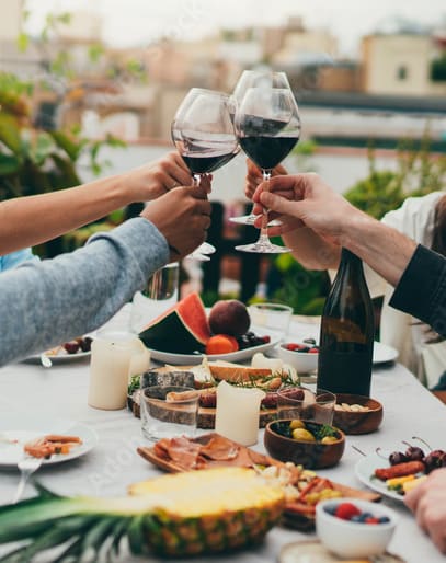 People toasting with wine glasses at a table with food.
