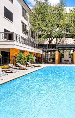 a swimming pool with chaise lounge chairs in front of an apartment building