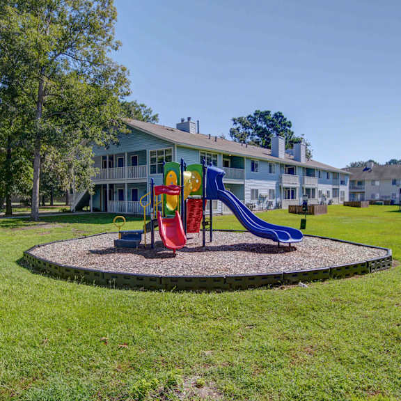A playground with a red slide and a blue slide in front of a building.
