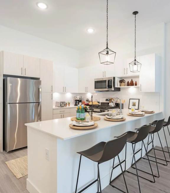 A modern kitchen with a white island and black barstools.
