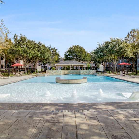 A large outdoor pool surrounded by trees and a fence.