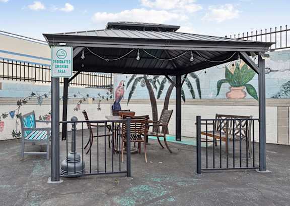 A patio with a table and chairs under a roof with a sign that says "Dedicated to the community".