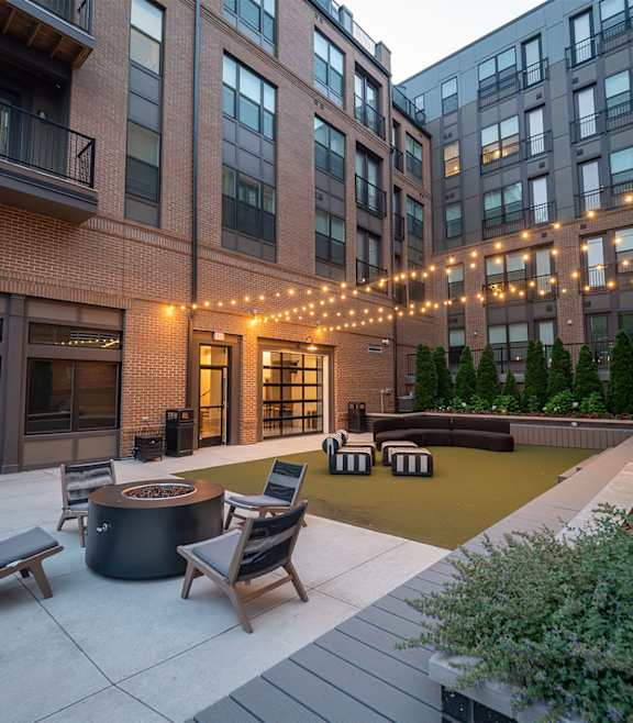 A patio with a fire pit and chairs is surrounded by buildings.