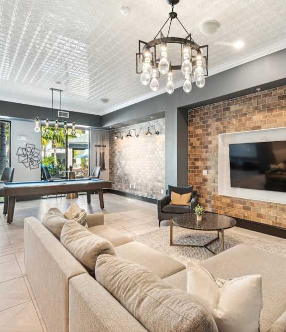 A living room with a large couch and a flat screen TV mounted on a brick wall at AxisOne Apartments in Stuart, FL 34994