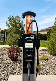 A Leviton electric vehicle charging station sits in a landscaped area.