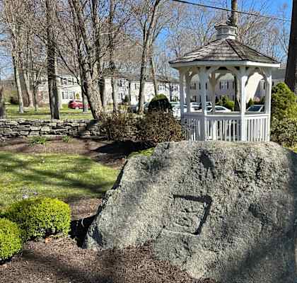 a large rock in a garden with a white gazebo