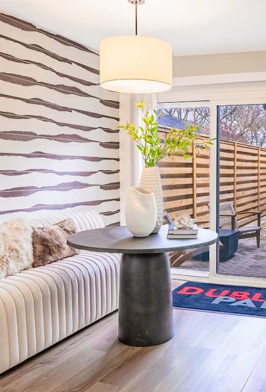 A living room with a white sofa, a black table, and a striped wallpaper.