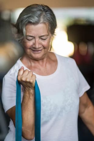 an older woman walking in a gym holding a resistance band