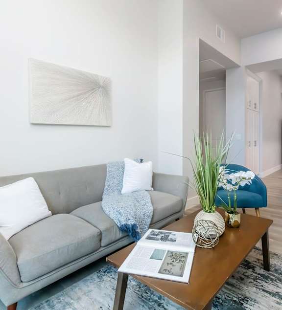 A living room with a grey couch and a painting on the wall.