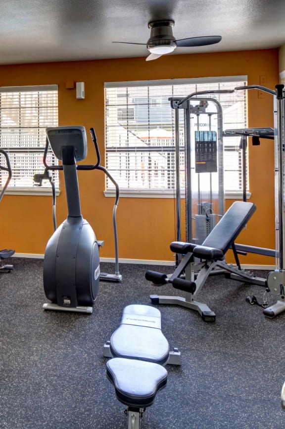 a gym with cardio equipment and weights in a building with orange walls at 2000 Lake Washington Apartments, Renton, WA, 98056