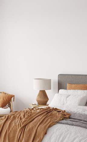 A bed with a grey headboard and white pillows is covered with a brown blanket.