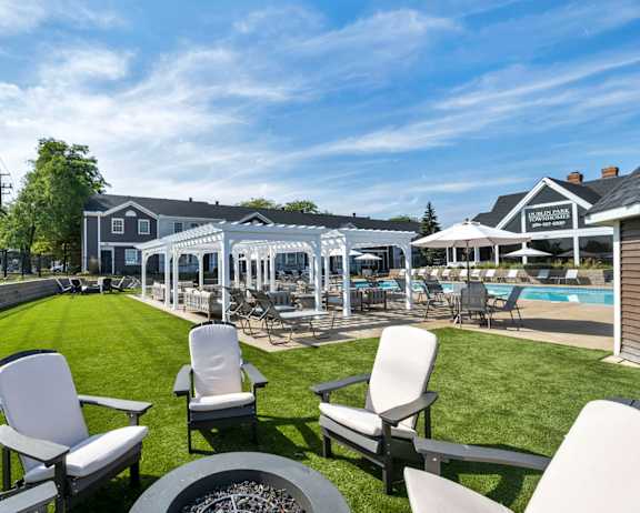 A lawn with chairs and a pool in the background.