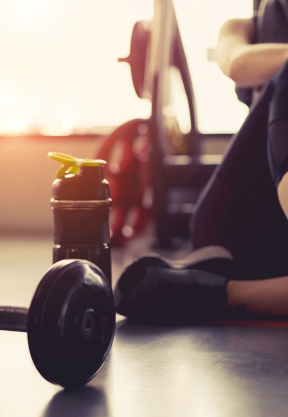 a woman sitting on the floor next to a dumbbell and water bottle