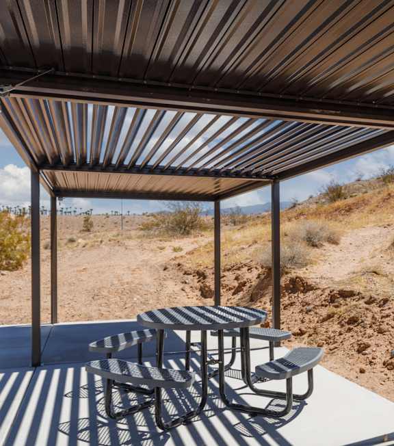 A metal patio structure with a table and chairs in a desert landscape.